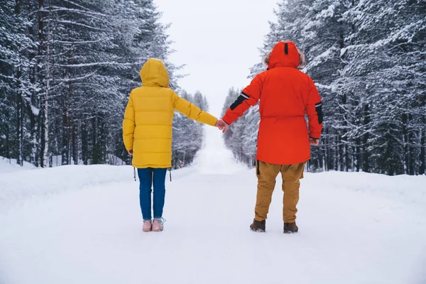 Back view of male and female couple in warm winter coats holding hands enjoying vacation together