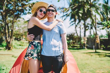 Yaz kıyafetleri ve güneş gözlükleriyle gezen mutlu gezginler. Tropik bir yerde kamp çadırının yanında balayının tadını çıkarıyorlar.