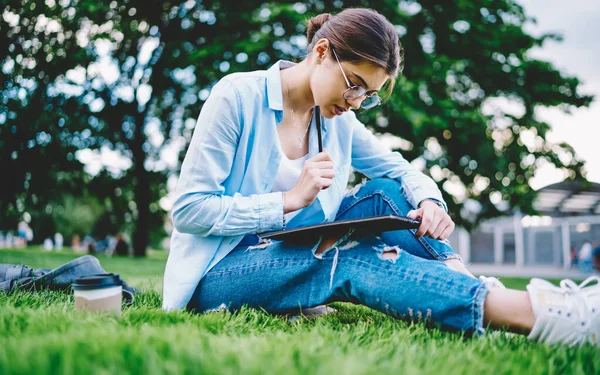 戴着光学眼镜的聪明女生正在阅读备考汇编 坐在草地上思考问题 — 图库照片