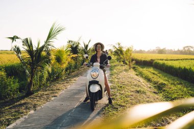 Eski moda scooter 'da poz veren çekici beyaz turistin portresi. Doğada güneşli havanın tadını çıkarıyor.