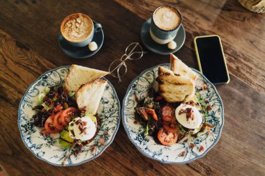 Lezzetli organik yemek, domates ve kızarmış ekmek, gözlük ve akıllı telefonun yanında bir fincan kahveyle servis ediliyor.