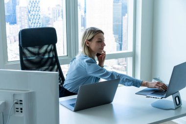 Bilgisayarlı ve dizüstü bilgisayarlı cep telefonuyla konuşurken dizüstü bilgisayarda yazan meşgul kadın yöneticinin yan görünümü