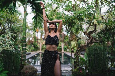 Havalı giysiler içinde esnek genç bir bayan kollarını kaldırmış ve tropik tatil beldesinde tatilin tadını çıkarırken kafasını arkaya atıyor.