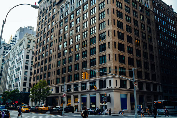 High stone tower with large windows on crossroad with driving taxis and public transport in downtown of New York City