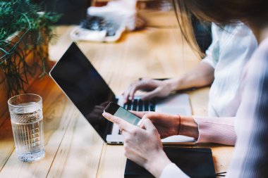 Gündüz vakti rahat bir kafede dizüstü bilgisayar projesinde çalışırken gündelik kıyafetlerini giymiş, ahşap masada oturmuş akıllı telefonlara göz gezdiren isimsiz arkadaşlar.