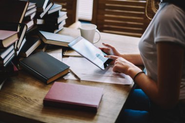 Yeni projede çalışırken arkadaşlarıyla mesajlaşan, kahve molasında tablet kullanan ve masada kitaplarla oturan kadınların yan görüntüsü