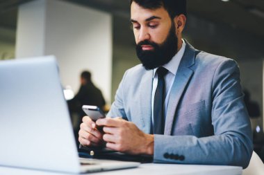 Gündüzleri dizüstü bilgisayar üzerinde çalışırken akıllı telefon kullanan şık takım elbiseli girişimci.