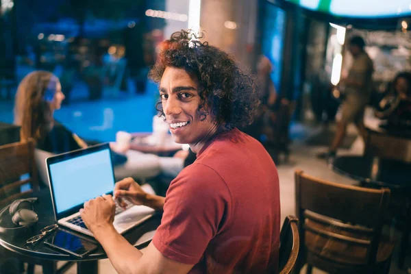 Portrait of smiling male freelancer 20s doing distance job on modern laptop technology sitting in cafeteria