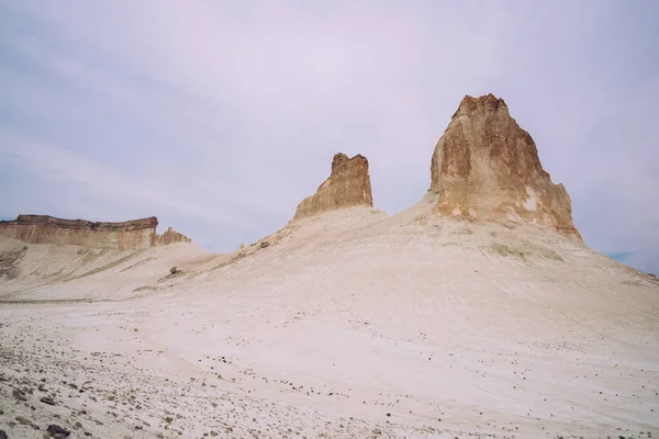乾燥した空の砂漠の谷の真ん中にそびえ立つ岩の峰の絵のような風景と白い砂の表面が石で覆われています — ストック写真