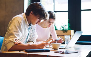 Kafede birlikte çalışırken bilgisayarlı masada oturan ve akıllı telefonları karıştıran konsantre arkadaşların yan görüntüsü