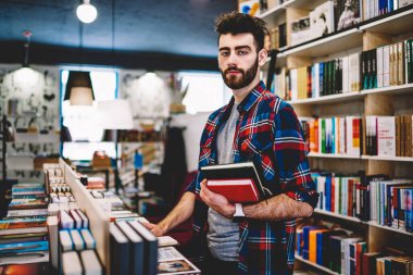 Yarım uzunluk portre zeki yakışıklı erkek genç üniversite kütüphanesinin rafları kitaplarla, zeki öğrenci bilgi ve belgeleri arama yaparken kameraya bakarak serbest zaman geçirmek