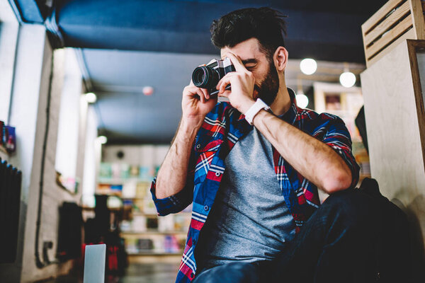 Young handsome male amateur photographer making pictures using vintage camera at university campus, caucasian hipster guy casual dressed taking photo with favourite retro technology indoors