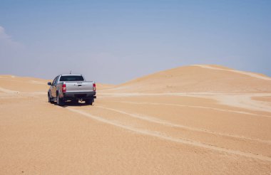 Yaz tatilinin güneşli bir gününde kumlu kum tepelerinde araba sürerken lastik izleri bırakan gümüş renkli bir kamyonet.