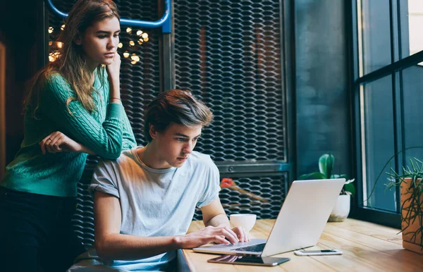 认真的女学生穿着绿色毛衣 靠着朋友的肩膀在现代笔记本电脑上打字 同时在当代咖啡馆里一起工作 — 图库照片
