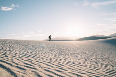 Kumlu kum tepecikleri üzerinde inanılmaz bir milli parkta yürüyen ve White Sands Ulusal Parkı 'nda akıllı telefon kullanan isimsiz bir erkek.