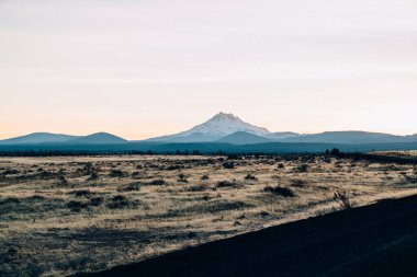 ABD 'de yaz akşamları açık gökyüzüne karşı karlı dağların yakınındaki kaya yığınlarıyla bomboş savanalar.