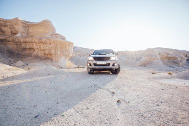 Modern otomobiller kayalık çölde, kumla kaplı, kayalık kayalık kayalıklarla ve mavi bulutsuz gökyüzüyle geziyor.