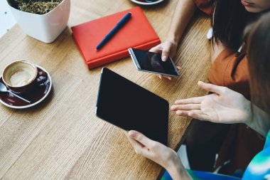 Masadaki kafede oturan, kahve fincanının yanında tablet ve telefon kullanan ve kalemle birlikte not defteri olan isimsiz bayan arkadaşlardan.