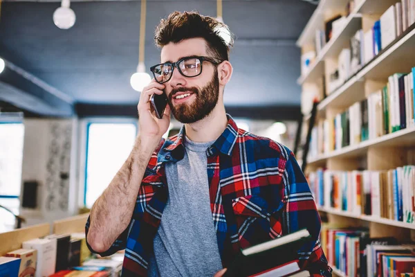 Neşeli sakallı hippi, elinde ders kitabı olan akıllı telefon cihazıyla arıyor. Gözlüklü şık genç bir öğrenci kütüphanede arka plandaki kitaplığın yanında cep telefonuyla konuşuyor.