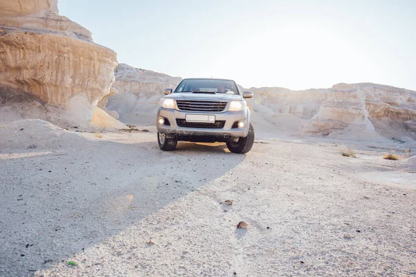 Picturesque view of dry rocky formations in canyon with uneven sandstone mountains with jeep parked under cloudless blue sky