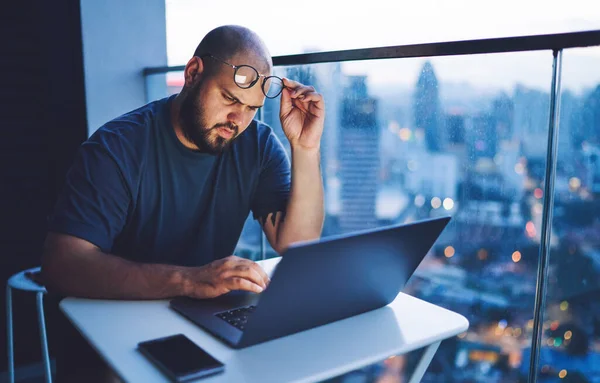 Pensive Male Freelancer Touching Eyeglasses Sitting Table Using Modern Laptop — стоковое фото