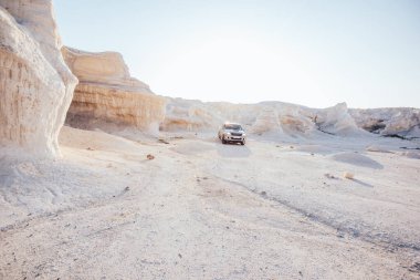 Kuru kumtaşı oluşumları ve güneşsiz yaz gününde çölde giden büyük araba ile kumlu kanyonun nefes kesici manzarası.