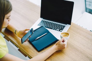 Kahvede otururken cep telefonu ihbarını kontrol eden, internet rehberi ve not defteri kullanan yüksek açılı bir kadın.