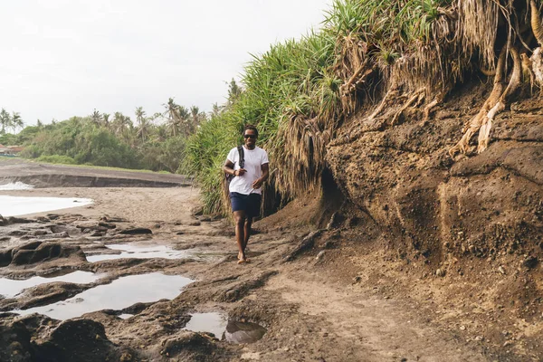 Yazın dalgalı deniz kıyısında sırt çantalı ve güneş gözlüklü, tanınmayan bir adamın vücudu.