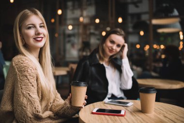 Modern kahve dükkanında akıllı telefonlu bir masada otururken gündelik giyinen şık kızlar kameraya bakıp kahve içmekten zevk alırlar.