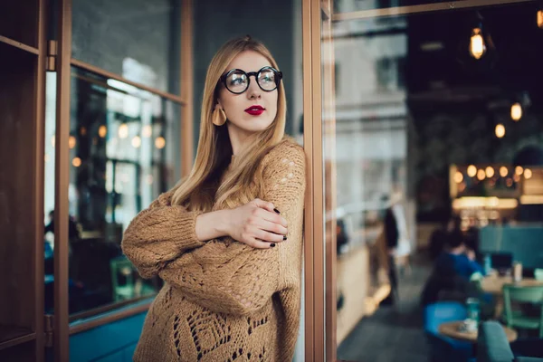 Günümüz kafesinde dikilen ve öğleden sonraları vakit geçirirken düşünceli bir kadın gözlüğü ve süveter giyiyor.