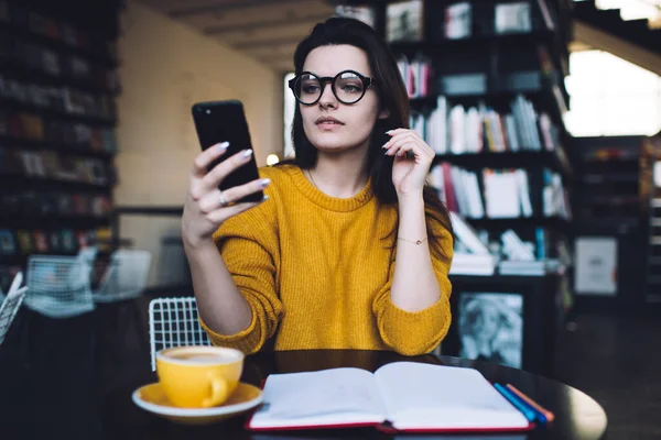 Concentrated Female Eyeglasses Sitting Black Table Bookshelf Using Cellphone While — Stock Photo, Image