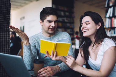 İyimser çift ders çalışırken konuşuyor ve gülüyor. Modern ofiste masada oturmuş sarı not defterinden notlar okuyorlar.