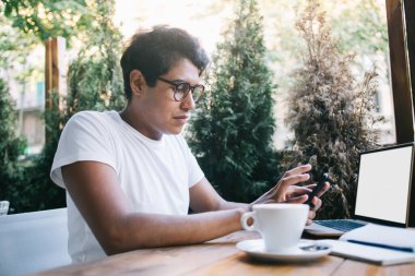 Kafe masasında oturan yetenekli erkek programcı grafik tasarımı ve modern cep telefonu aygıtı için fotokopi alanı alanı ile dizüstü bilgisayarı hazırlıyor.