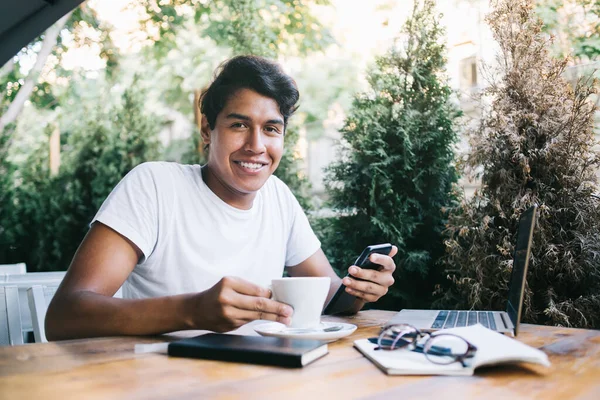 Portrait of cheerful software developer holding coffee cup and modern cellphone technology in hands