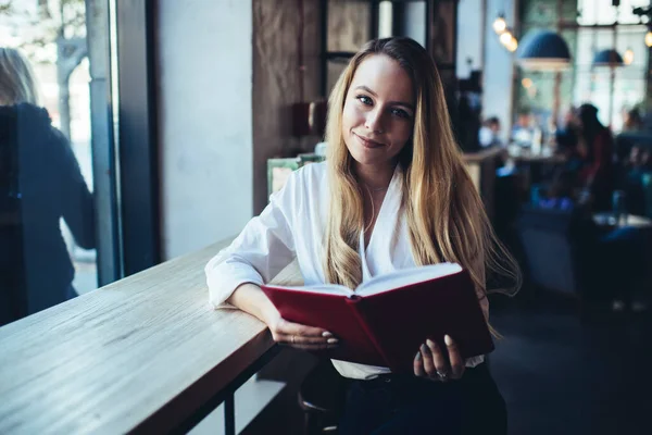 Młoda Szczęśliwa Blondynka Białej Bluzce Czytająca Książkę Siedząca Przy Stole — Zdjęcie stockowe