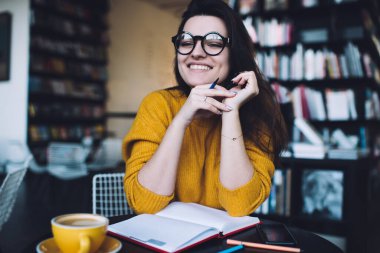Genç, bardaklı, hardal kazaklı, elinde kalemle masada oturmuş bir fincan kahvenin tadını çıkarıyordu.