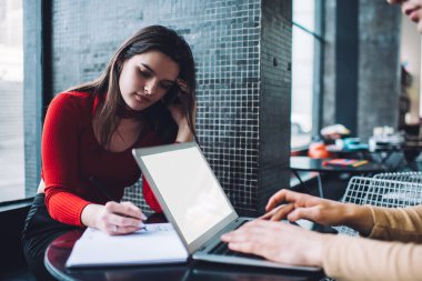 Düşünceli kadın not defterine not alıyor. İş arkadaşıyla aynı masada oturuyor ve gündüzleri rahat iş yerinde dizüstü bilgisayarda klavye kullanıyor.