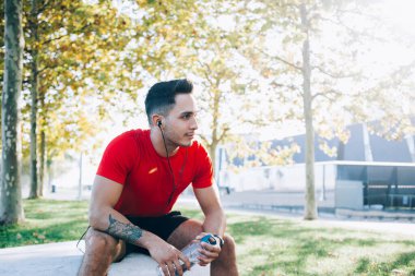 Elinde su şişesi olan koşucu idman molası sırasında elektronik kulaklıkla ses kayıtlarını dinliyor.