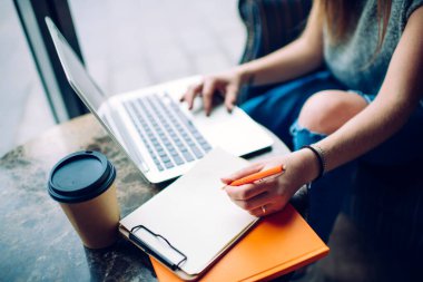 Tahta masada oturmuş, dizüstü bilgisayarını karıştırıp not alan, sıradan kıyafetli, isimsiz bir kadın serbest yazar.