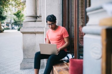 Optik gözlüklü Latin erkek programcı 4G internet bağlantısı olan dizüstü bilgisayar kullanıyor.