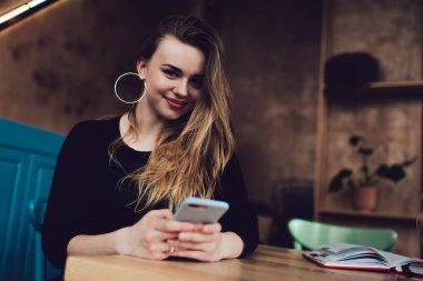 Rahat bir kafede cep telefonuna bakarken gülümseyen ve kameraya bakan sıradan bir kadının düşük açılı pozitifi.