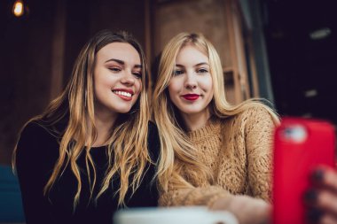 Rahat bir kafede oturup cep telefonuyla selfie çeken rahat rahat giyinen kadınların düşük açısı.
