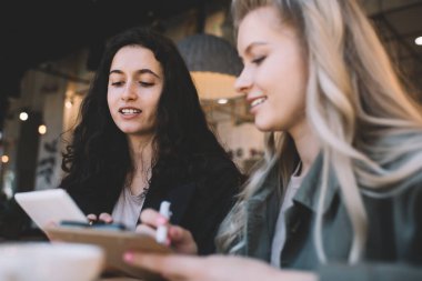 Tablet kullanan ve panoya not alan iyimser genç bayan meslektaşlar masada toplanıyor ve modern çalışma alanında birlikte başlangıç projesi üzerinde çalışıyorlar.