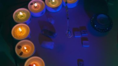 Karma arındırma töreni. Kader kehaneti, gül kuvars kristalleri, sarkaç, rünler, mum ışığında aroma mumları. Arka planda tütsü çubukları.