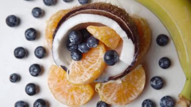 Hindistan cevizinin yarısının içindeki yabanmersini ve portakal dilimleri. Beyaz yüzeydeki muz ve böğürtlen. Meyve seti. 