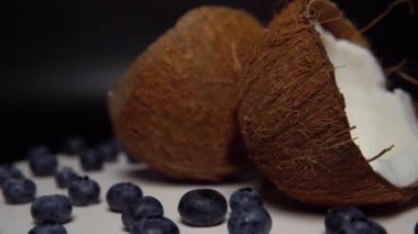 The handful of fresh blueberry and halves of coconut on the black background.