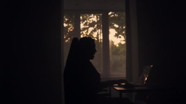 The joyful adult guy is saying hello to his friend on the video chat. Call with friend. Sunset and trees in the window on the background.