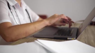 The adult woman physician is working in the cabinet at clinic with white walls.
