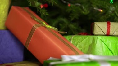 A lot of presents for Christmas holiday under the fir-tree in green, purple, yellow and orange gift wrap.