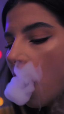 The girl smokes a vape releases a lot of steam. Color light. Vertical video. High quality FullHD footage
